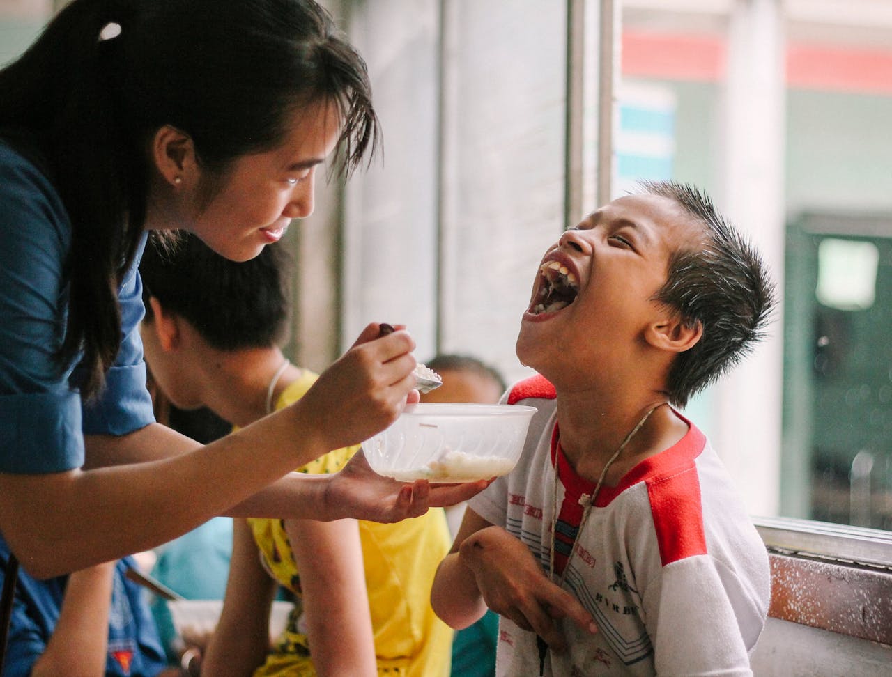 Joyful moment as a woman feeds a happy child in a warm, indoor setting.